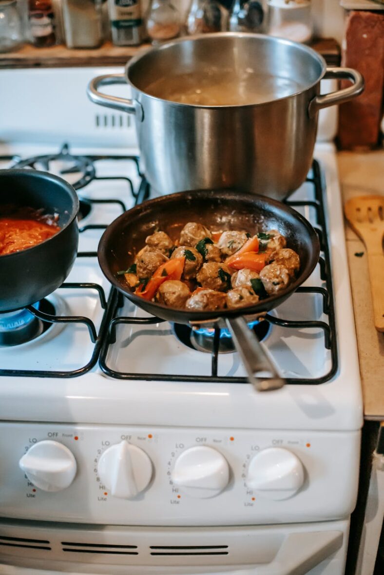 pan with saucy meatballs frying on gas stove in kitchen Fogão a Gás o guia definitivo