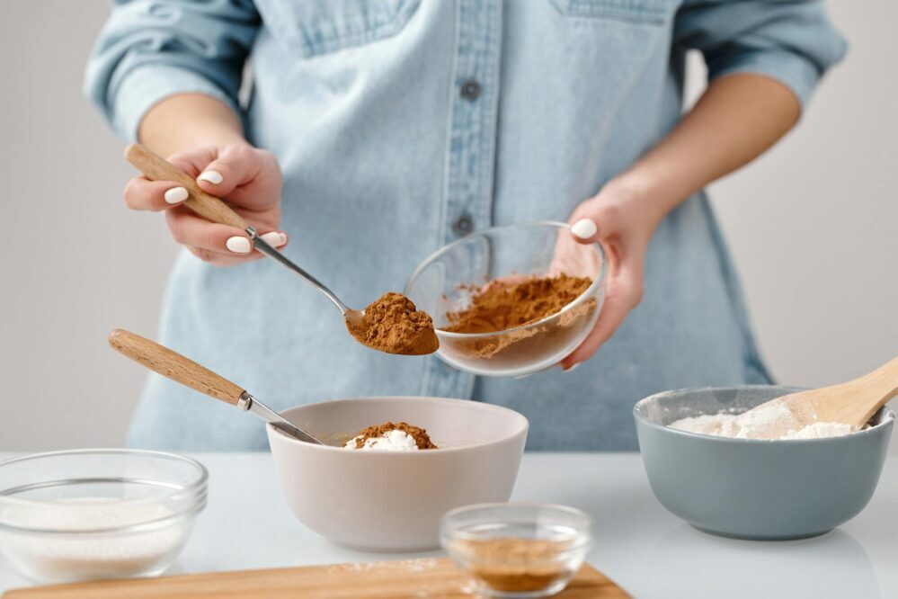 person adding a spoon of cinnamon in a bowl Medidas das Colheres veja as Diferenças