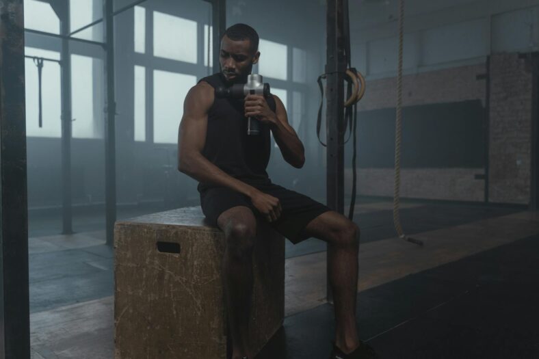 a fit man using a massage gun on his shoulder