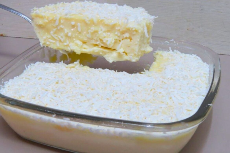Taça com sobremesa gelada de coco cremosa, superfície lisa e brilhante, finalizada com coco ralado em flocos e fio de leite condensado.
