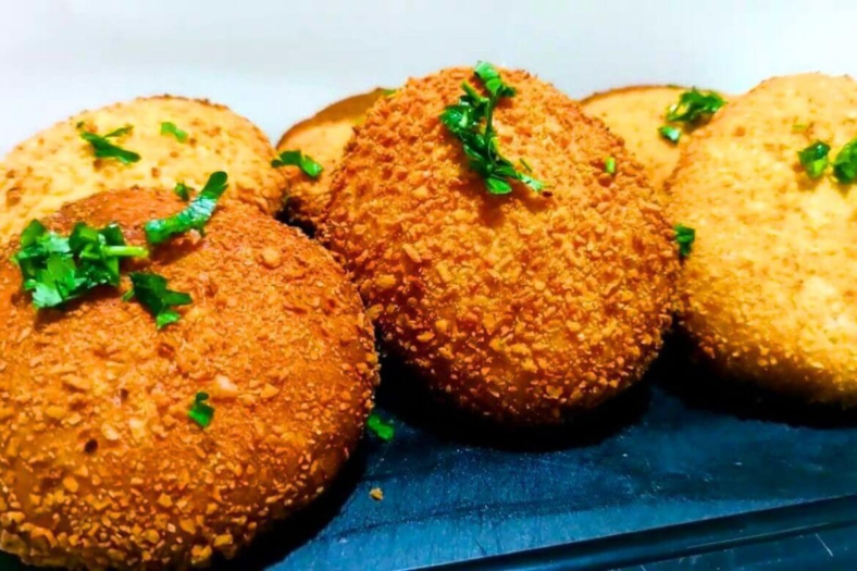Salgados fritos dourados e crocantes de queijo e presunto empanados com farinha panko, servidos em uma cesta com molhos para acompanhar.