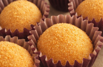 Brigadeiros de paçoca em forminhas marrons, cobertos com amendoim moído grosso, dispostos em uma bandeja rústica com elementos de festa junina ao fundo.