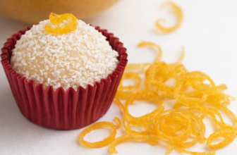 Brigadeiros de limão siciliano em forminhas brancas, cobertos com açúcar cristal e raspas de limão, dispostos em uma bandeja rústica com limões sicilianos ao fundo.