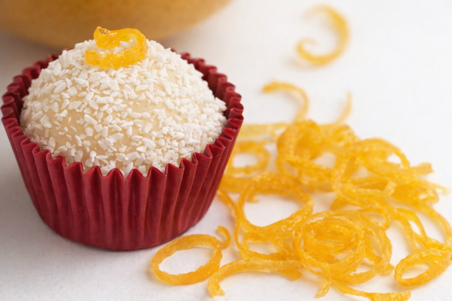 Brigadeiros de limão siciliano em forminhas brancas, cobertos com açúcar cristal e raspas de limão, dispostos em uma bandeja rústica com limões sicilianos ao fundo.