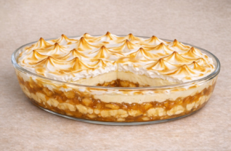 Travessa com Chico Balanceado, mostrando as camadas: caramelo de banana, creme branco e merengue dourado com picos decorativos.