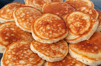 Tareco Bolinhos de frigideira dourados e fofinhos empilhados em um prato, acompanhados de uma xícara de café e um pano de prato xadrez ao fundo.