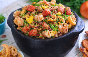 Travessa com feijão tropeiro mineiro, grãos de feijão envoltos em farinha, pedaços de torresmo crocante, linguiças e couve fatiada.