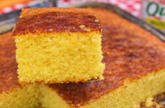 Bolo de milho cremoso em forma de buraco no meio, com superfície dourada e fatia servida em prato branco ao lado de uma xícara de café.