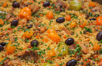 Panela com galinhada mineira, pedaços de frango dourado, arroz soltinho, bacon crocante, cenoura e pimentões coloridos, finalizada com salsinha fresca.