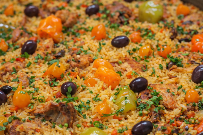 Panela com galinhada mineira, pedaços de frango dourado, arroz soltinho, bacon crocante, cenoura e pimentões coloridos, finalizada com salsinha fresca.