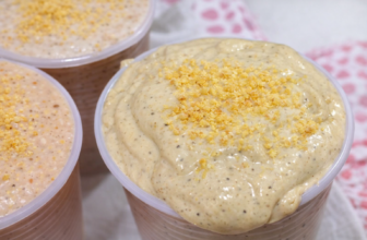 Copo grande com bebida cremosa de guaraná da Amazônia, textura aveludada, finalizada com canela em pó e acompanhada de castanhas ao fundo.