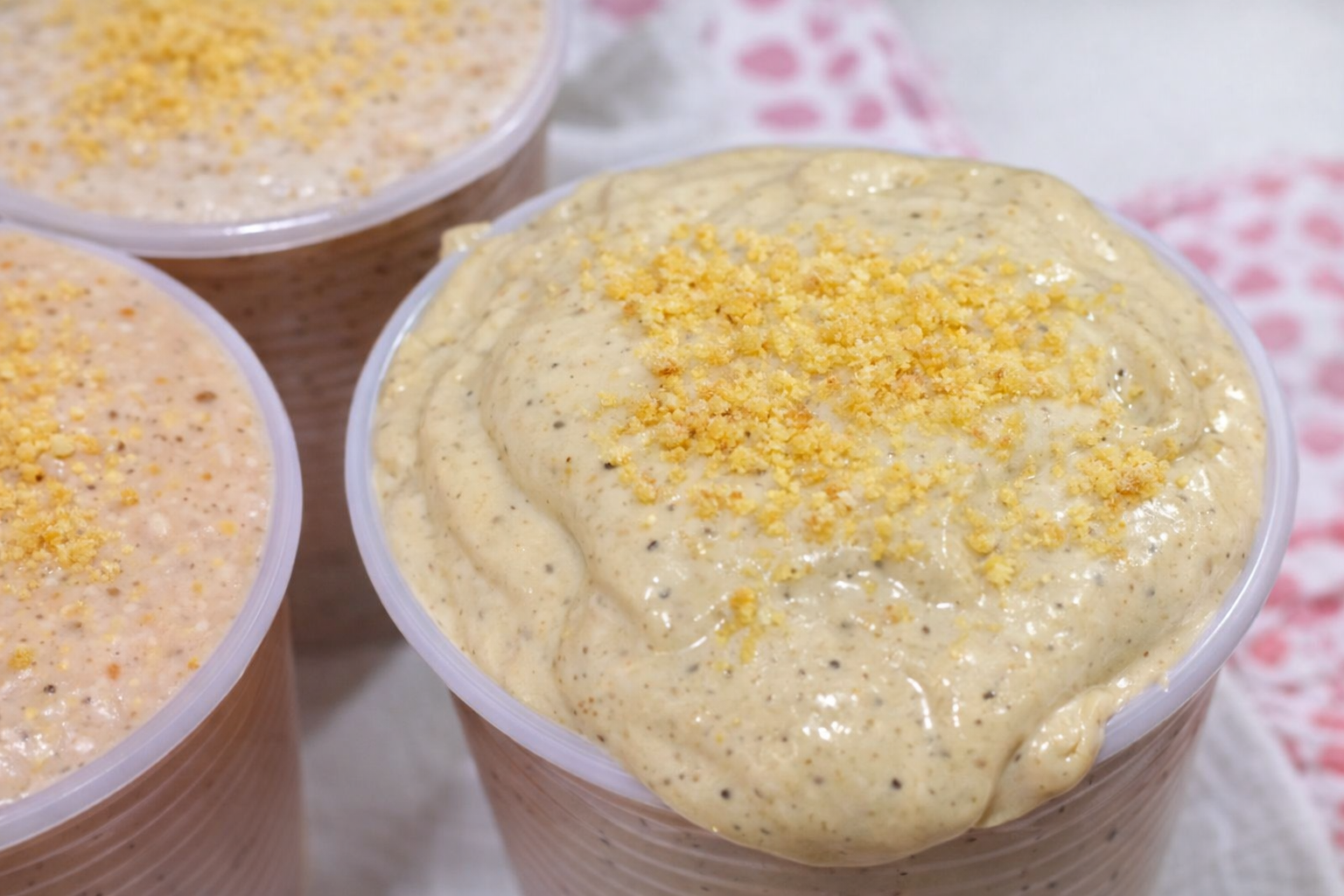 Copo grande com bebida cremosa de guaraná da Amazônia, textura aveludada, finalizada com canela em pó e acompanhada de castanhas ao fundo.
