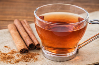Xícara de chá de canela sobre superfície bege, acompanhada de paus e pó de canela, com iluminação natural suave.