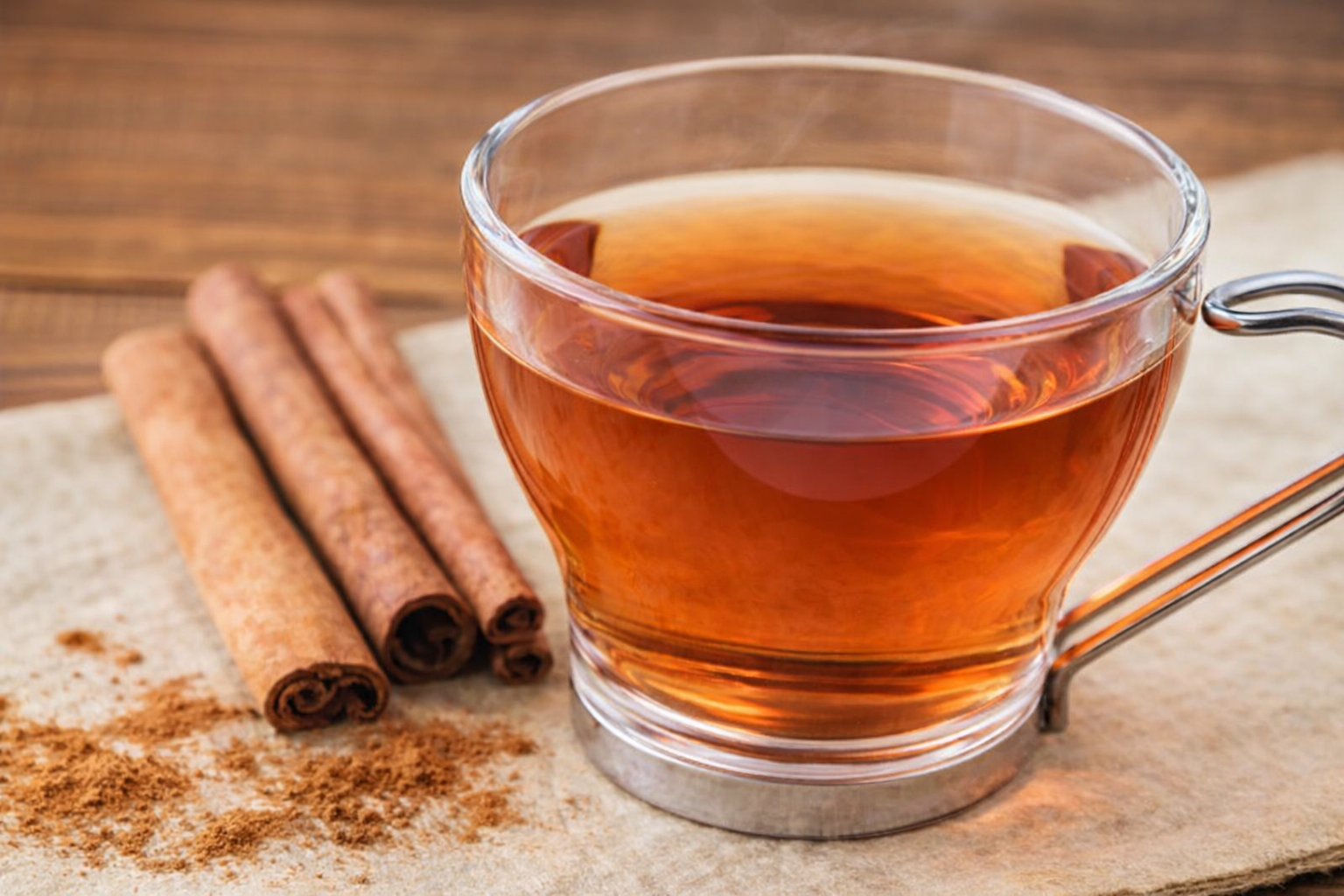 Xícara de chá de canela sobre superfície bege, acompanhada de paus e pó de canela, com iluminação natural suave.
