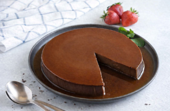 Flan de chocolate brilhante em prato escuro com morangos frescos e folhas de hortelã ao lado.